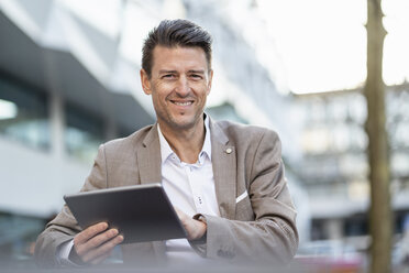 Porträt eines lächelnden Geschäftsmannes, der im Freien ein Tablet benutzt - DIGF06496