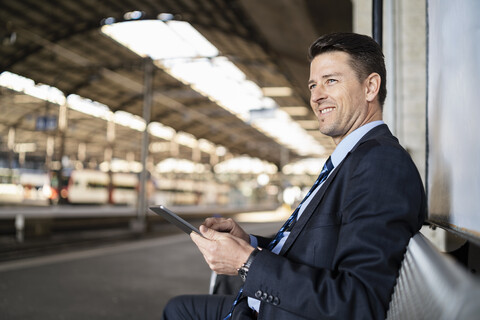 Lächelnder Geschäftsmann mit Tablet wartet auf dem Bahnsteig, lizenzfreies Stockfoto