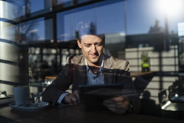 Businessman using tablet behind the window in a cafe - DIGF06500