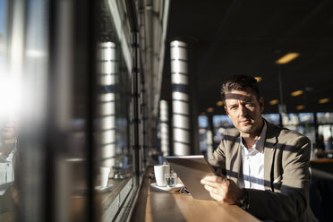Porträt eines Geschäftsmannes, der ein Tablet am Fenster eines Cafés benutzt - DIGF06502