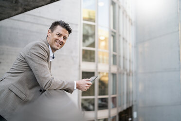 Portrait of smiling businessman with tablet leaning on railing - DIGF06514