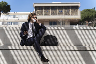 Italien, Florenz, junger Geschäftsmann, der ein Smartphone mit Kopfhörern im Freien benutzt - FMOF00507