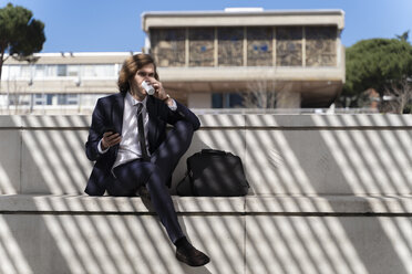 Italy, Florence, young businessman using smartphone with earbuds outdoor - FMOF00507