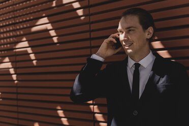 Lächelnder junger Geschäftsmann auf Smartphone im Freien - FMOF00526