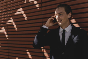 Smiling young businessman on smartphone outdoor - FMOF00526