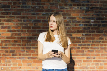 Junge Frau vor einer Backsteinmauer, mit Smartphone - GIOF06053