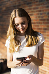Junge Frau vor einer Backsteinmauer, mit Smartphone - GIOF06055