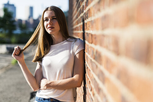 Junge Frau lehnt an einer Backsteinmauer in New York City - GIOF06060