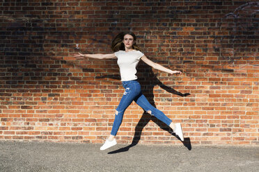 Agile young woman jumping in front of brick wall - GIOF06062