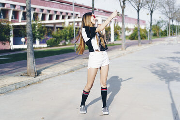 Spain, happy teenage girl ustaking a selfie on a road - ERRF00832