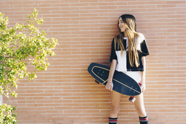 Spain, teenage girl holding skateboard at a brick wall - ERRF00839
