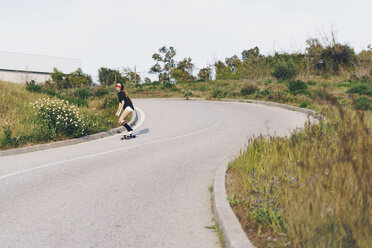 Spain, teenage girl riding skateboard down a road - ERRF00843