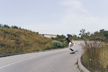 Spain, teenage girl riding skateboard down a road - ERRF00845