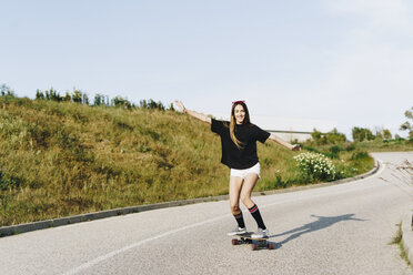 Spain, happy teenage girl riding skateboard down a road - ERRF00847