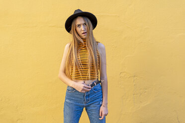 Portrait of annoyed teenage girl wearing hat at yellow wall - ERRF00884