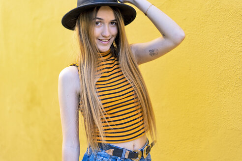 Porträt eines lächelnden Teenager-Mädchens mit Hut an einer gelben Wand - ERRF00888
