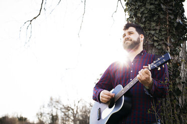 Mann spielt Gitarre an einem Baum auf einer Wiese - HMEF00267