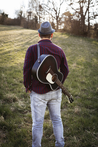 Rückansicht eines Mannes mit Gitarre, der auf einer Wiese steht, lizenzfreies Stockfoto