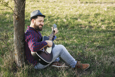 Mann spielt Gitarre an einem Baum auf einer Wiese - HMEF00277