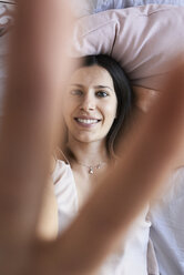 Porträt einer lächelnden jungen Frau auf dem Bett liegend mit Siegeszeichen, Ansicht von oben - IGGF00936