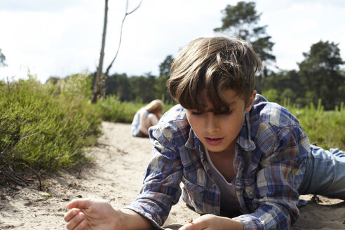 Boy lying on sandy path watching beetle - AMEF00055
