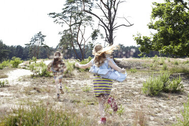 Rückansicht von zwei Mädchen, die durch eine Dünenlandschaft laufen - AMEF00057