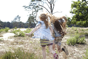 Rückansicht von zwei Mädchen, die durch eine Dünenlandschaft laufen - AMEF00058