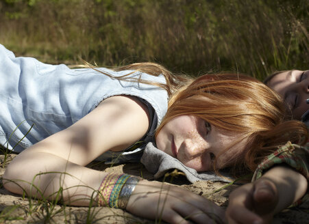 Portrait of redheaded girl lying on sandy soil - AMEF00059