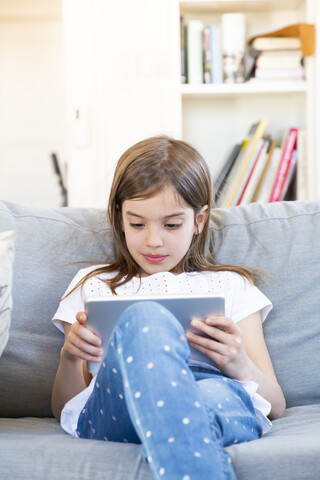 Portrait of little girl sitting on the couch at home using digital tablet stock photo