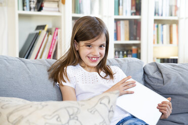 Porträt eines glücklichen kleinen Mädchens, das zu Hause auf der Couch mit einem digitalen Tablet sitzt - LVF07957