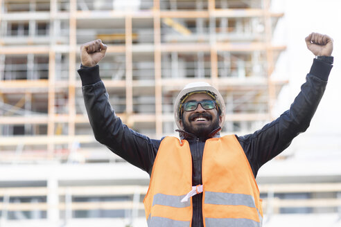 Porträt eines glücklichen Bauingenieurs vor einer Baustelle mit Schutzhelm und Sicherheitsweste - SGF02341