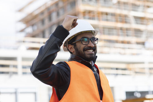Porträt eines glücklichen Bauingenieurs vor einer Baustelle mit Schutzhelm und Sicherheitsweste - SGF02342