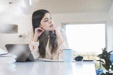 Young woman sitting at table at home looking sideways - UUF16938