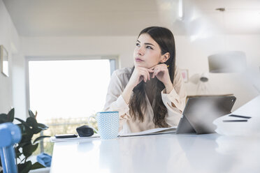 Young woman sitting at table at home looking sideways - UUF16939