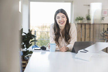 Happy young woman sitting at table at home - UUF16940