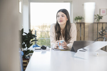 Young woman sitting at table at home thinking - UUF16941