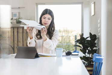 Young woman sitting at table at home holding plane model - UUF16947