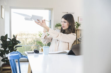 Young woman sitting at table at home holding plane model - UUF16948