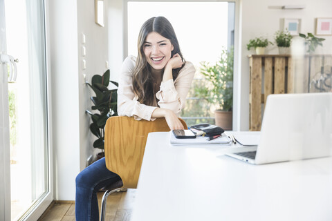 Portrait of happy young woman sitting at table at home stock photo