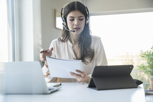 Young woman sitting at table at home wearing a headset - UUF16973