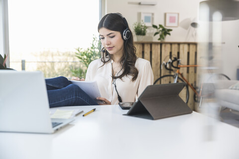 Young woman sitting at table at home wearing a headset stock photo