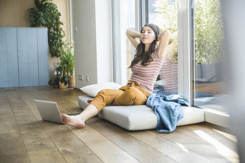 Entspannte junge Frau am Fenster sitzend zu Hause mit Laptop, lizenzfreies Stockfoto