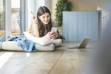 Young woman lying at the window at home using cell phone - UUF16986