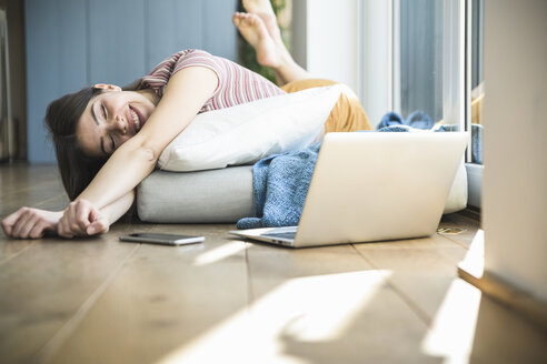 Relaxed young woman lying at the window at home with laptop - UUF16995