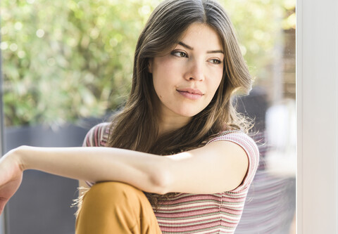 Portrait of pensive young woman sitting at the window at home stock photo