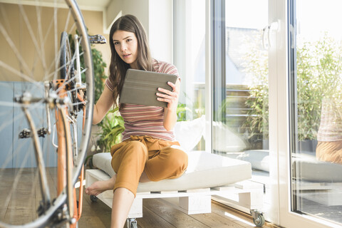 Junge Frau mit Tablet repariert Fahrrad zu Hause, lizenzfreies Stockfoto