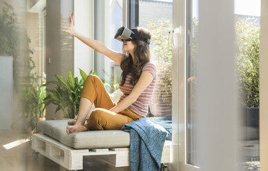 Young woman sitting at the window at home wearing VR glasses - UUF17022