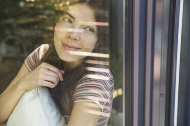 Porträt einer lächelnden jungen Frau hinter einer Fensterscheibe - UUF17026