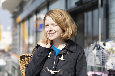 Porträt einer lächelnden Frau mit Einkaufstasche vor einem Supermarkt - SGF02350