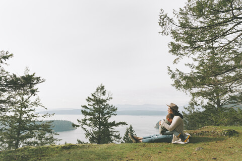 Mutter sitzt im Gras und kuschelt mit ihrem Sohn in der Natur, lizenzfreies Stockfoto